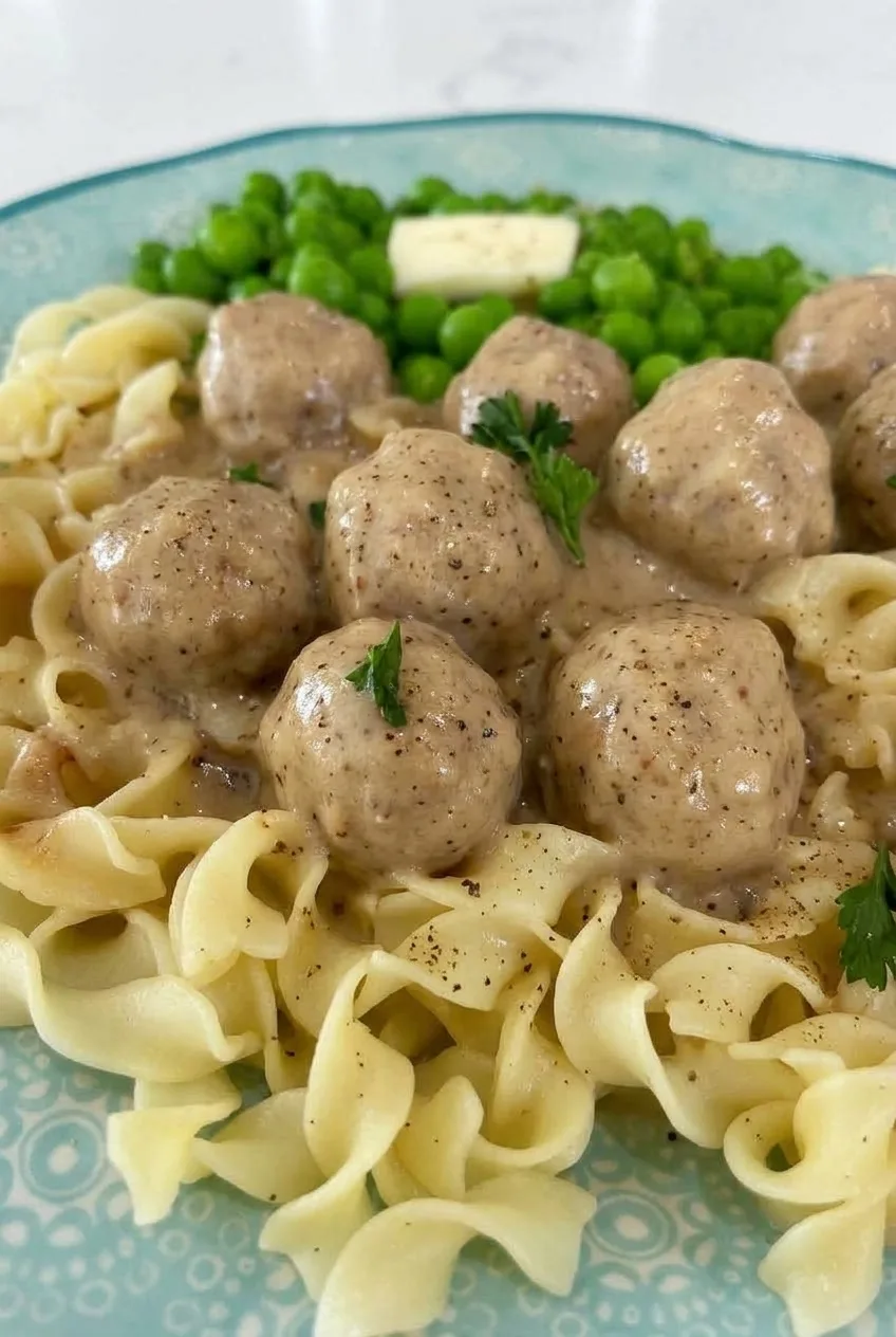 Close view of creamy gravy coating Swedish meatballs above distinct folds of egg noodles