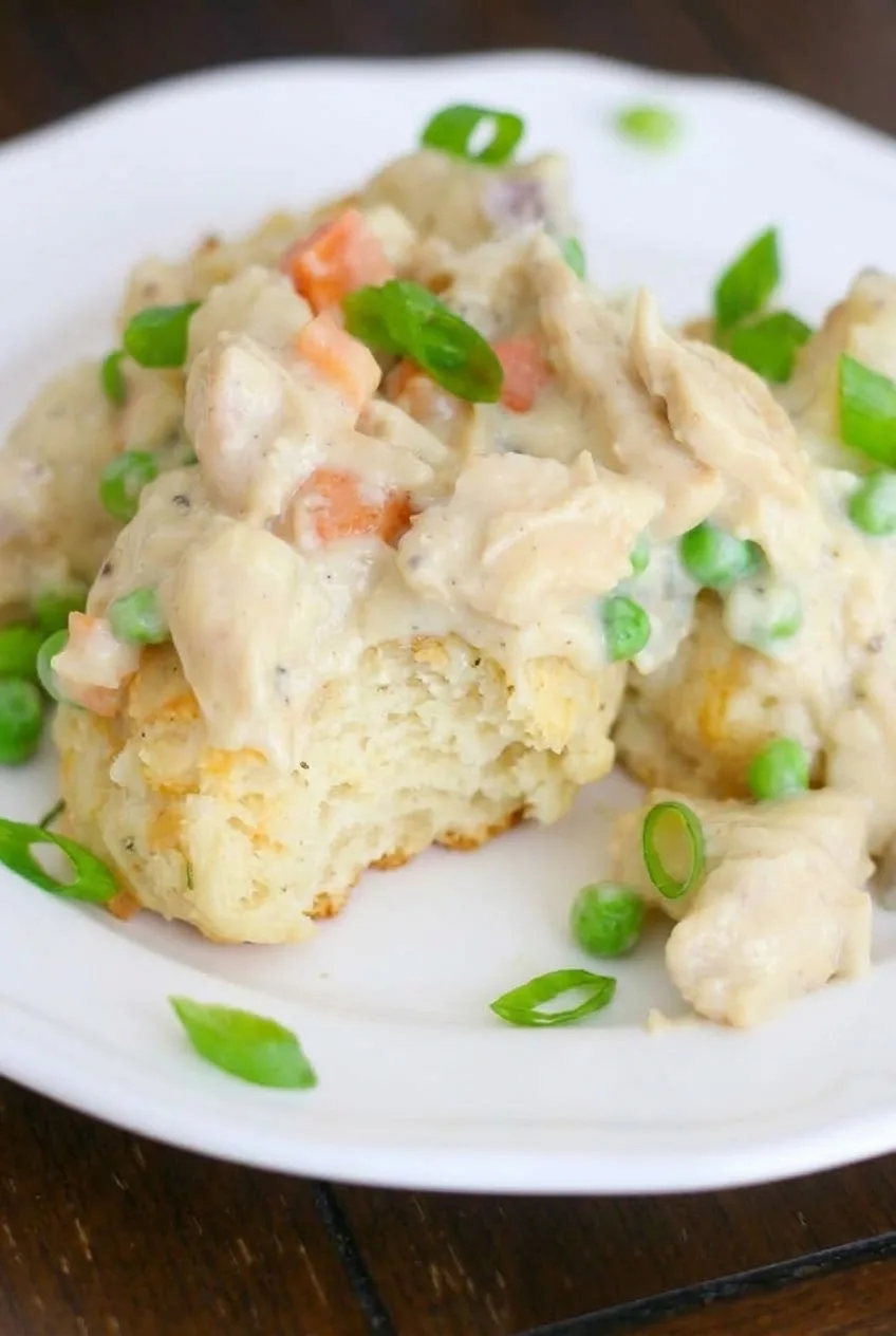 Close view of fluffy biscuit beneath creamy chicken, potatoes, peas, carrots, and green onions