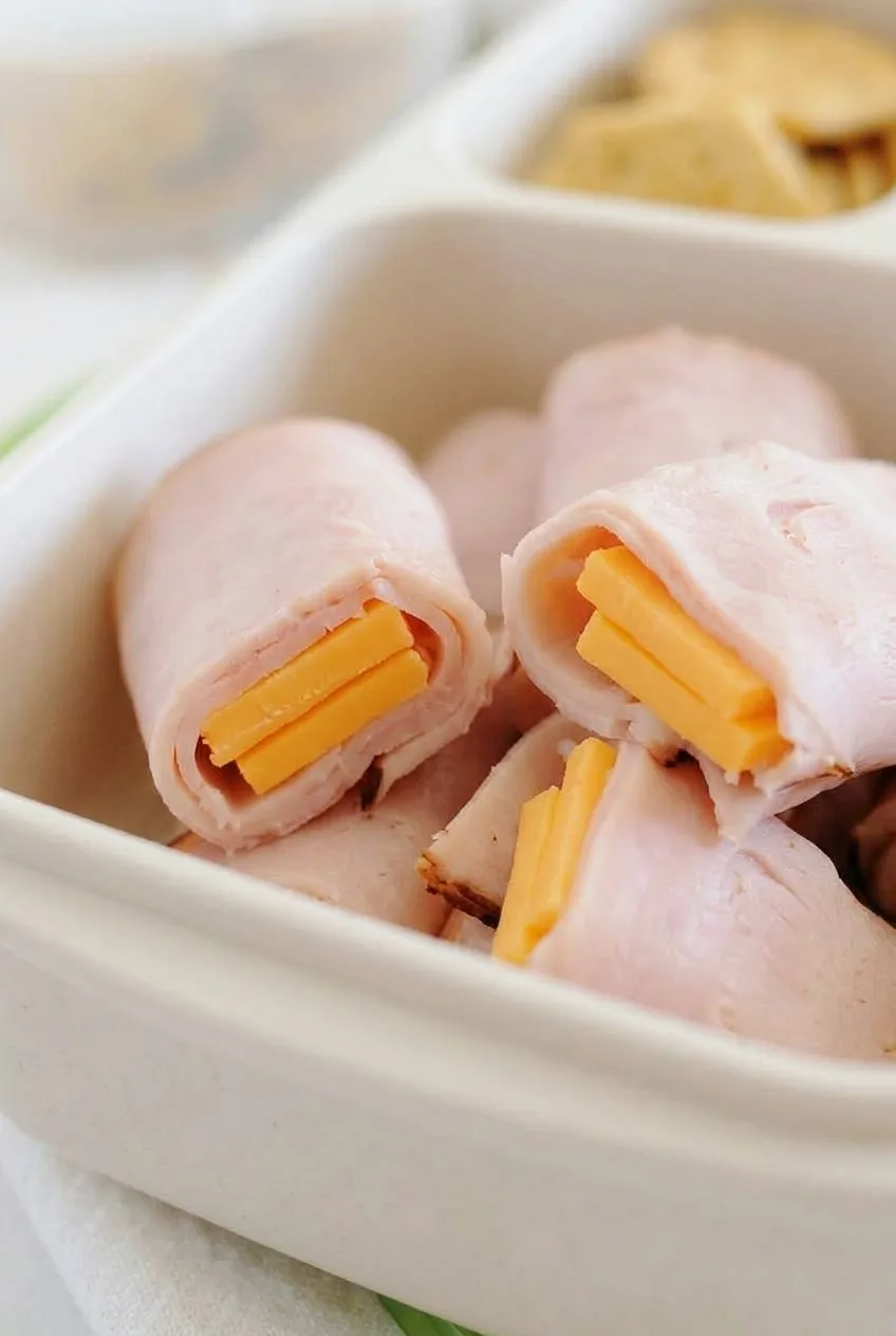 Close view of pale pink ham wrapped around orange cheddar in short lunchbox rolls