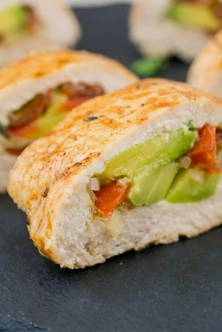 Close view of sliced avocado and tomato inside a thick cut of fully cooked chicken