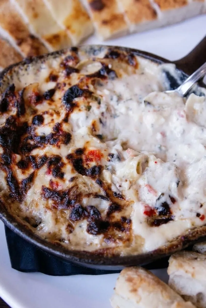 Close view of chunky crab dip beneath patchy browned cheese, opened with a spoon