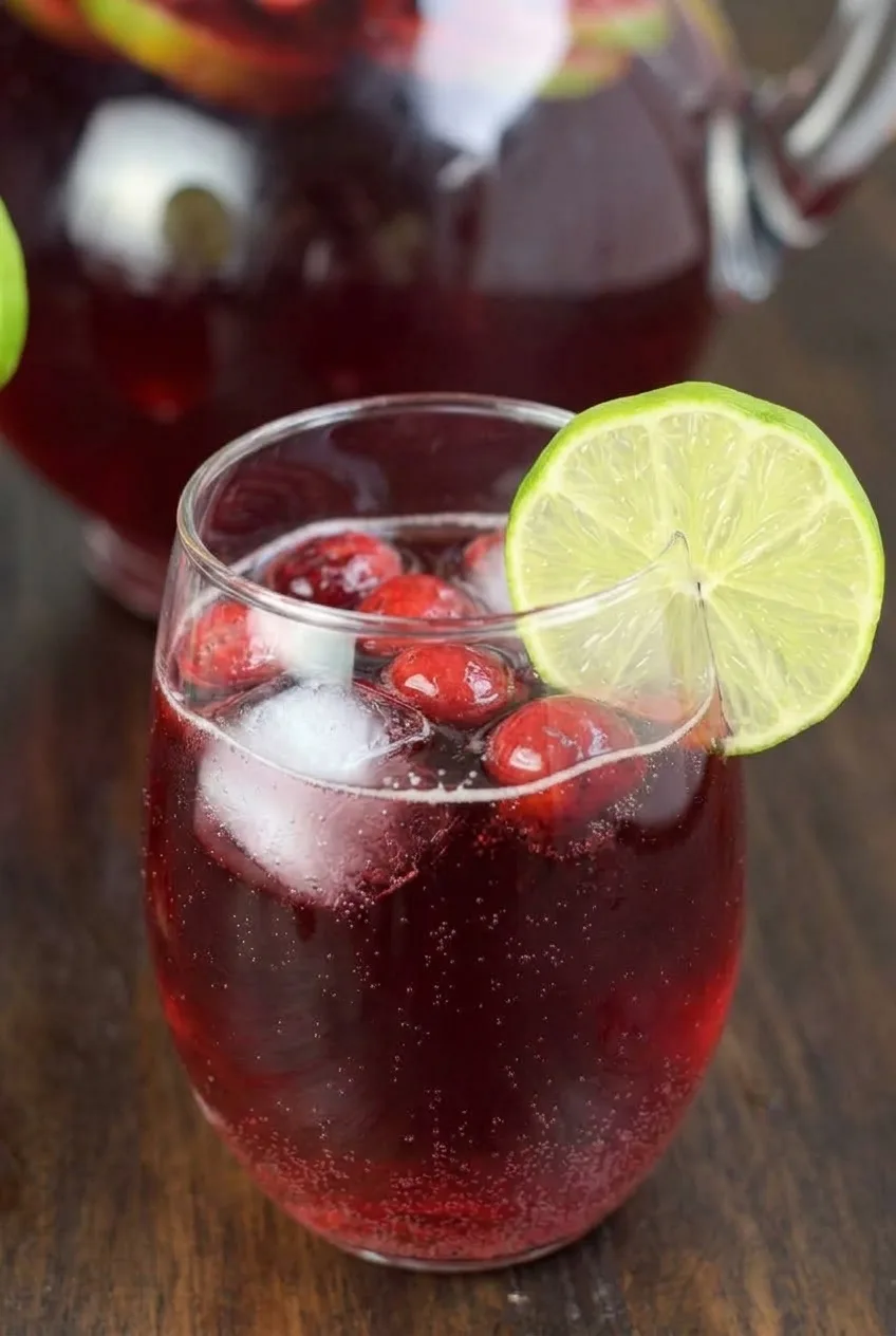 Close view of bubbles, ice and whole cranberries in ruby-red punch beneath a lime wheel