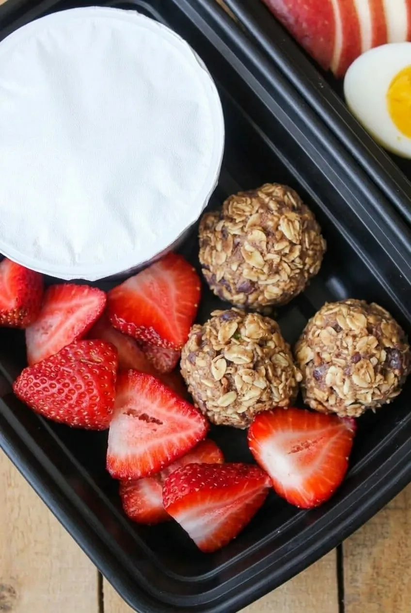 Close view of three textured oat bites beside cut strawberries and a sealed yogurt cup