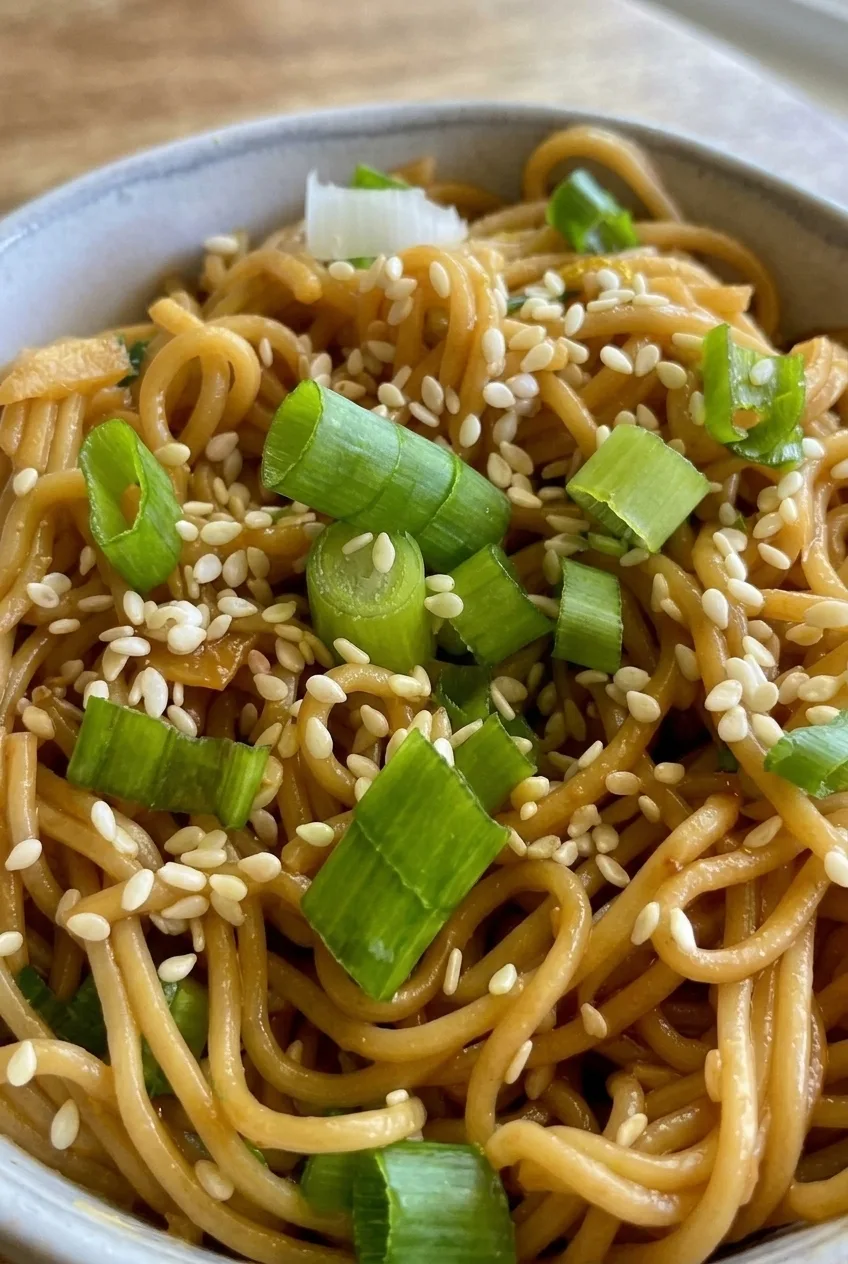 Close view of glossy ramen strands with white sesame seeds and chunky green onion slices