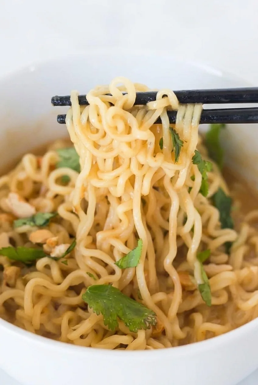 Close view of glossy peanut sesame ramen strands with chopped peanuts and cilantro