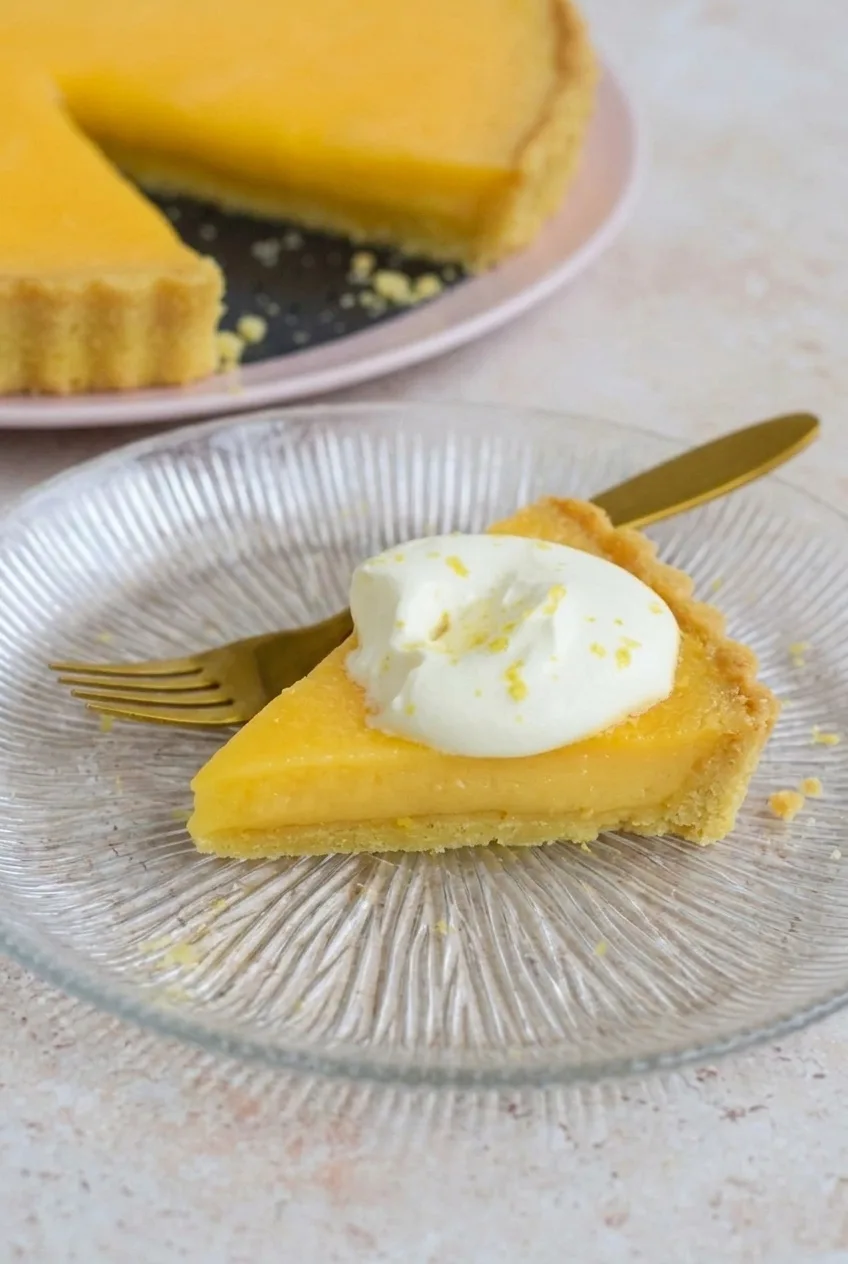 Close view of a French lemon tart slice showing smooth filling, thin pastry and whipped cream
