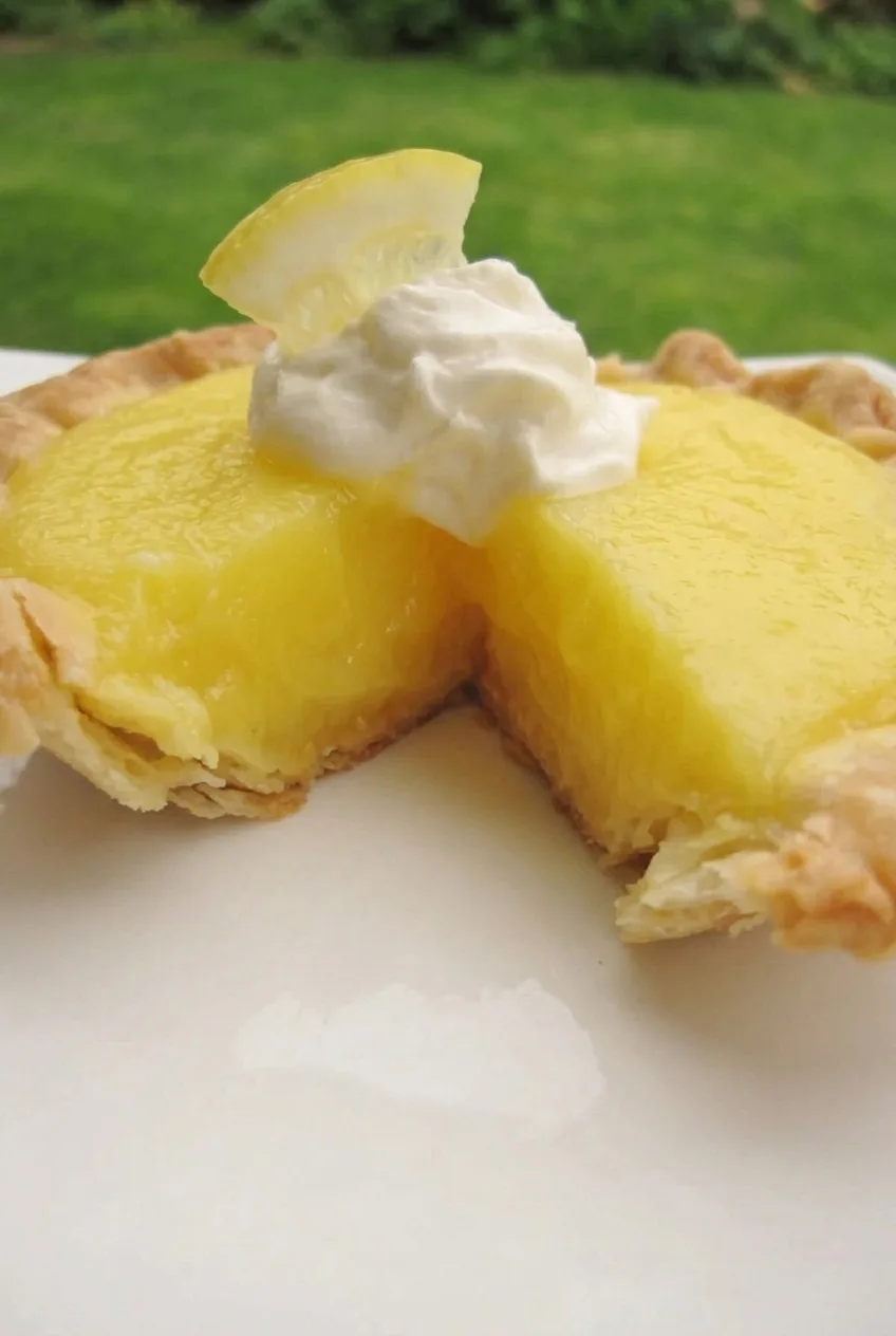 Close view of a mini lemon pie’s smooth cut filling, flaky crimped crust, and white meringue dollop
