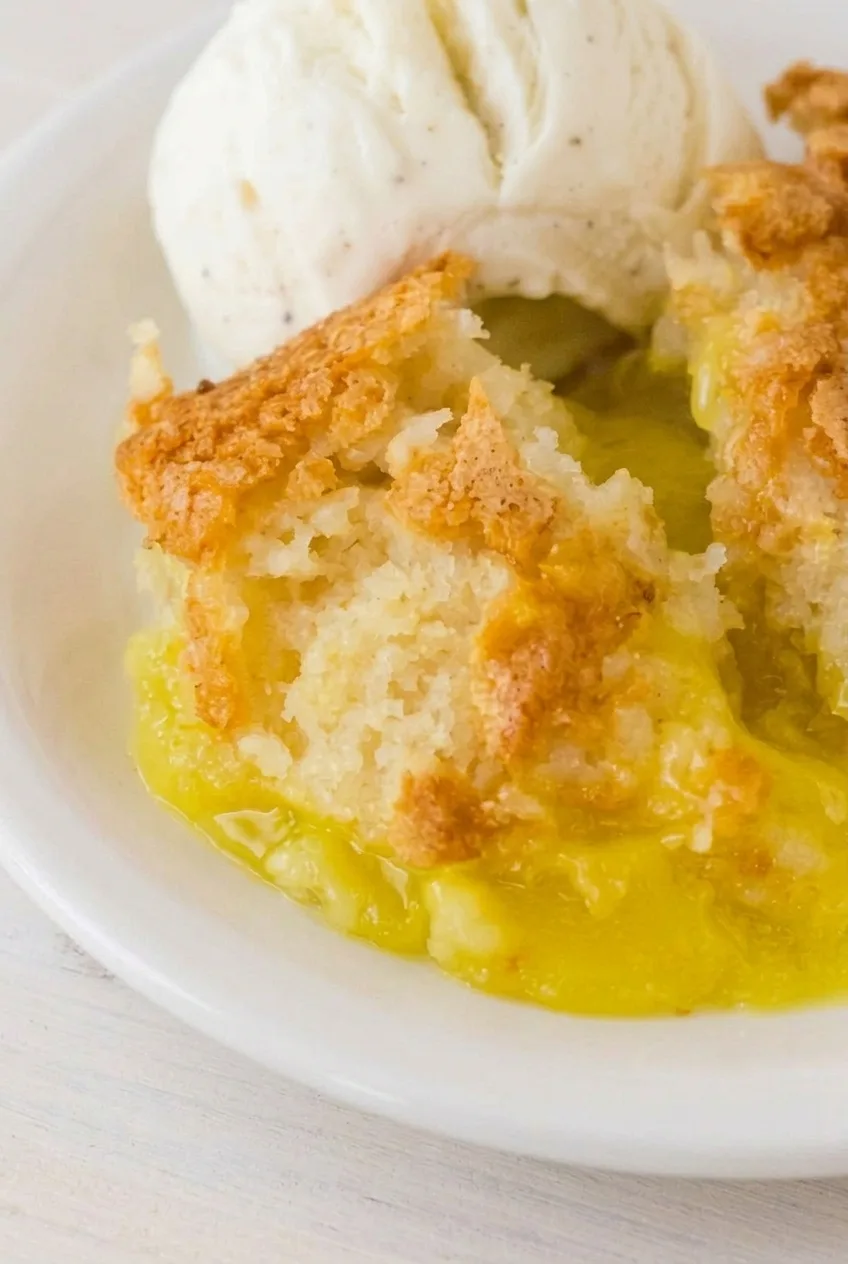 Close view of lemon cobbler's pale cake crumb and glossy yellow filling, with vanilla ice cream beside it