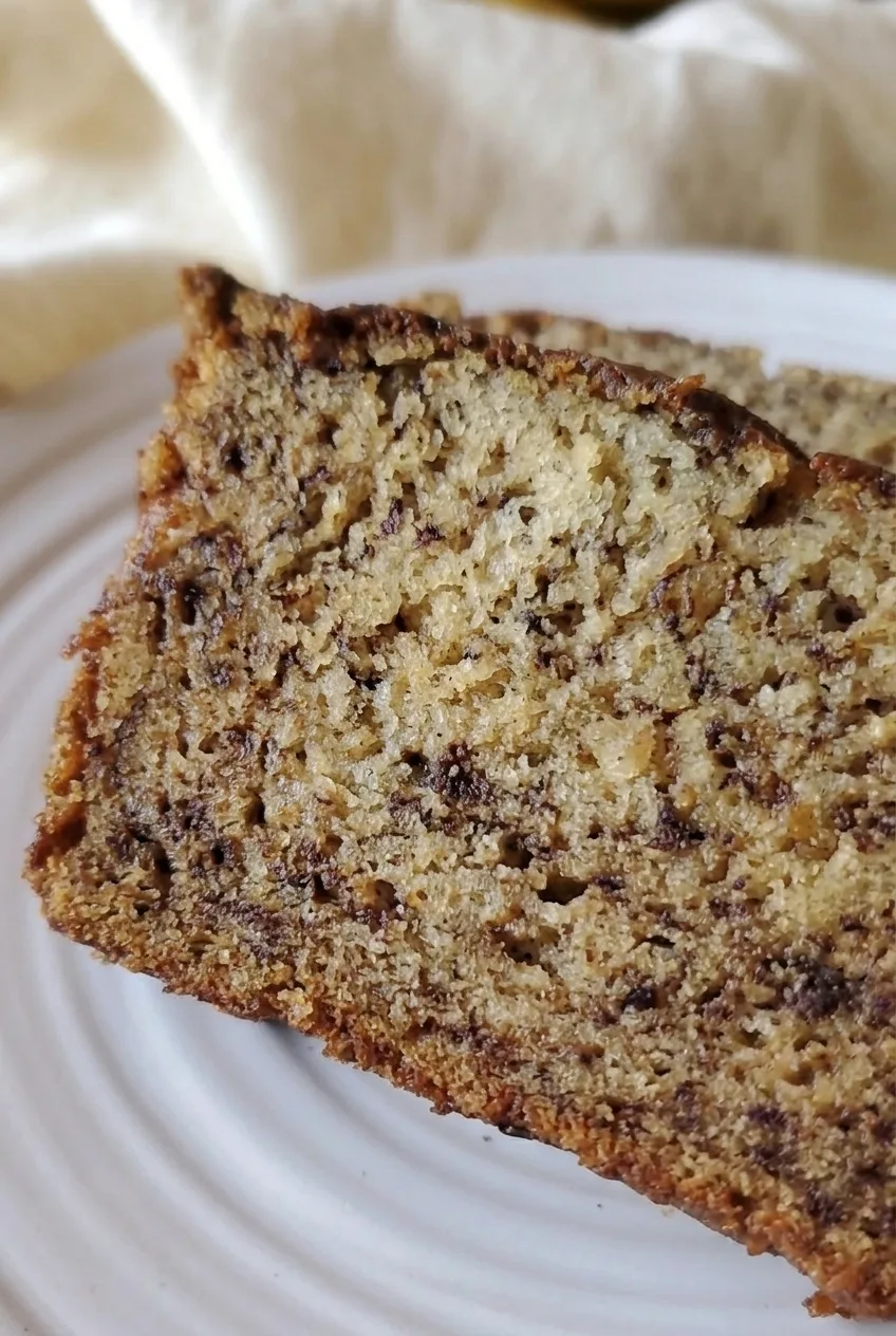 Close view of the moist, banana-flecked crumb and browned crust of a gluten-free banana bread slice