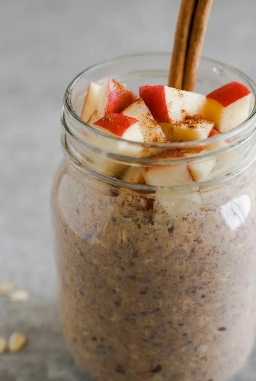 Close view of cinnamon-flecked oats through the jar and fresh apple pieces on top