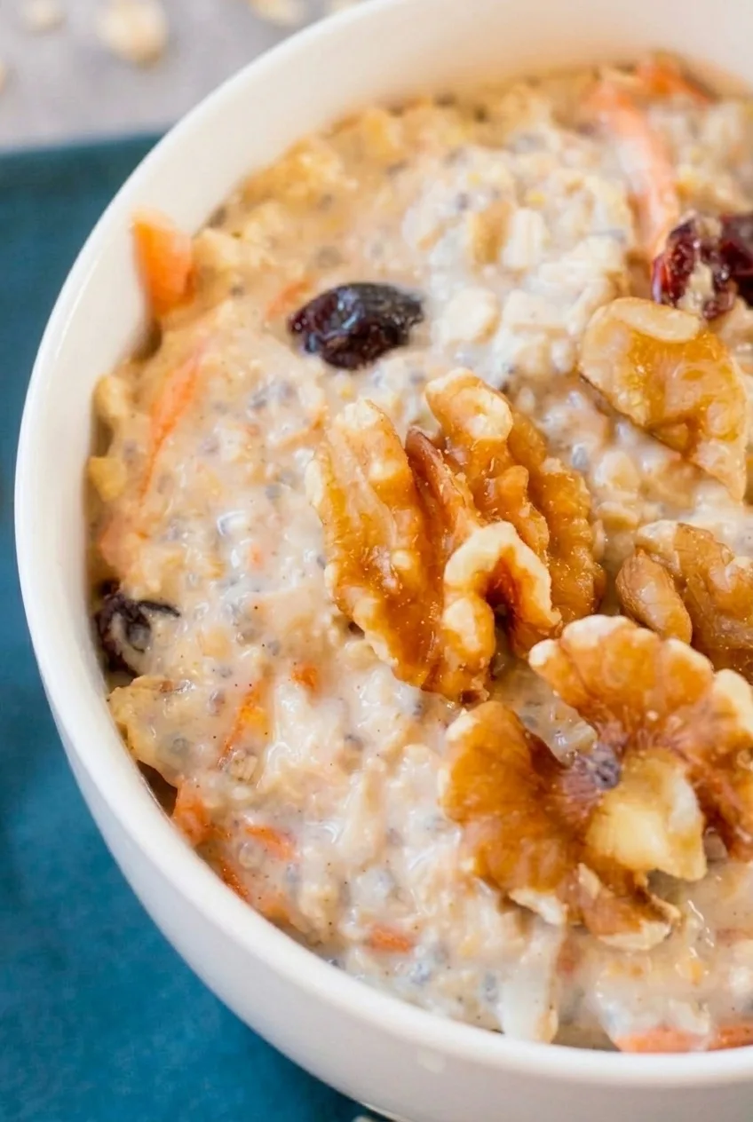 Close detail of softened oats, fine carrot shreds, raisins, and a walnut piece in a creamy bowl