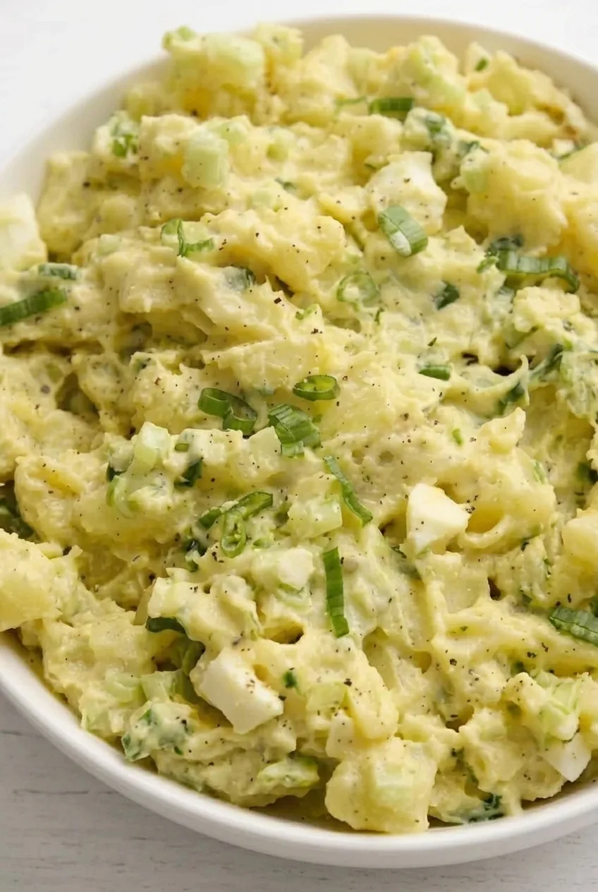Close view of potato and egg pieces coated in thick dressing with celery and green onion