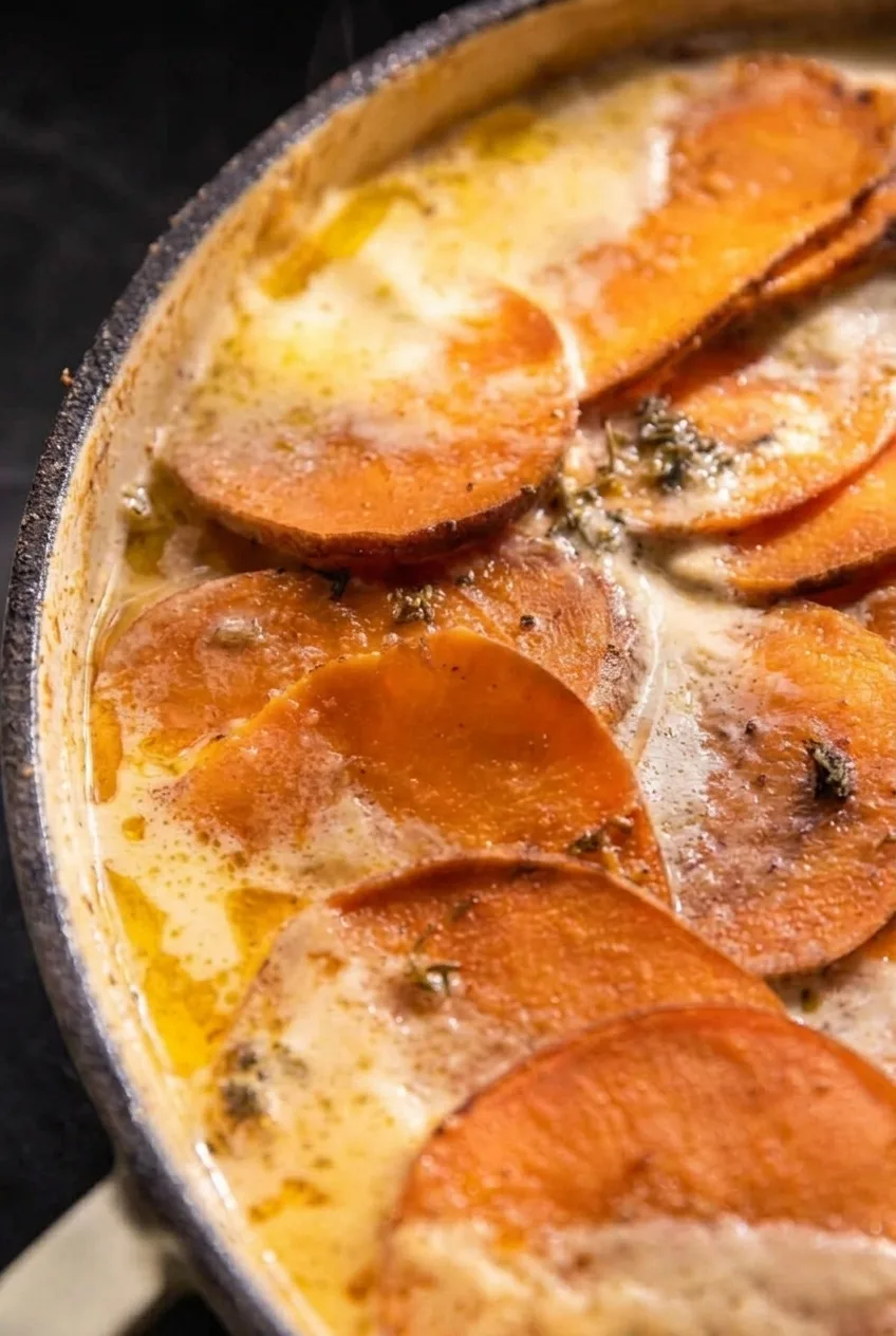 Close view of overlapping sweet potato rounds with browned edges and cream pooling between the slices