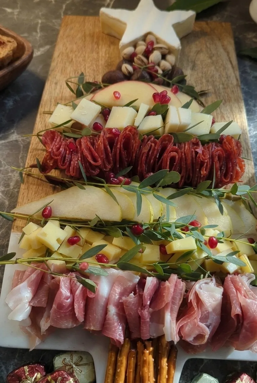 Close view of folded salami, prosciutto, sliced fruit, herbs, and pomegranate on the charcuterie tree