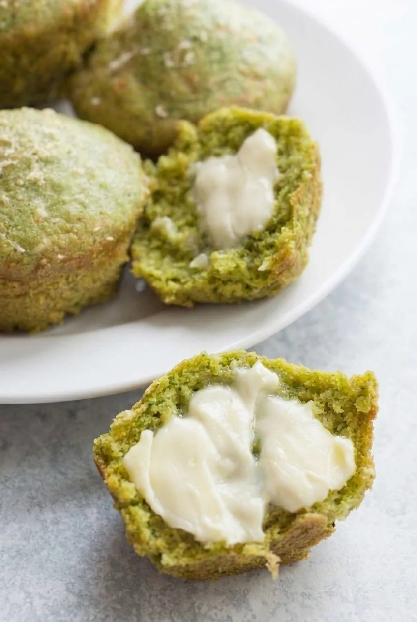 Close view of a buttered egg muffin split open to show its set interior and fine spinach flecks