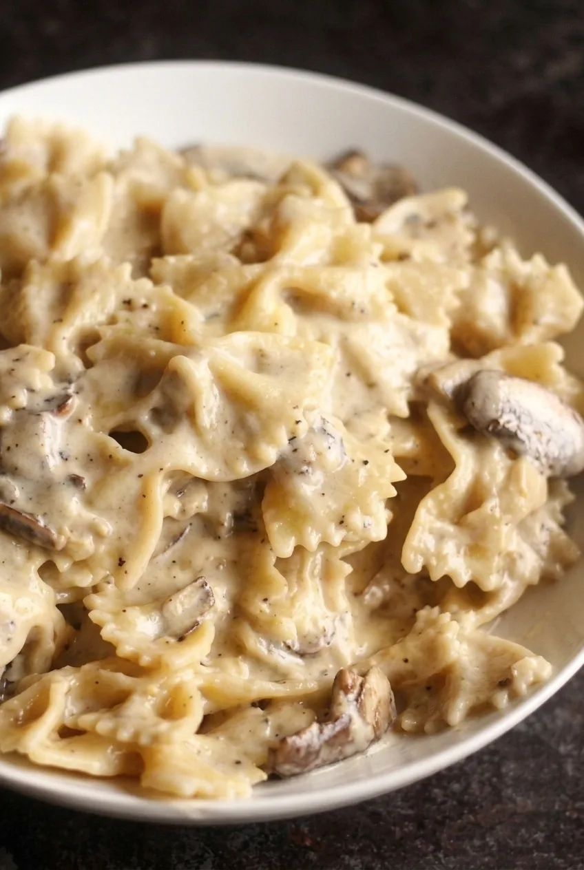 Close detail of creamy farfalle folds and tender sliced mushrooms coated in Parmesan cream sauce.