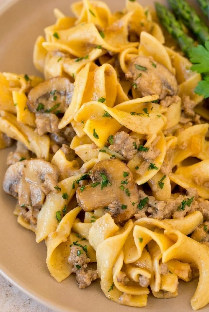 Close-up of creamy ground beef stroganoff showing folded egg noodles, mushroom slices, beef crumbles, and parsley