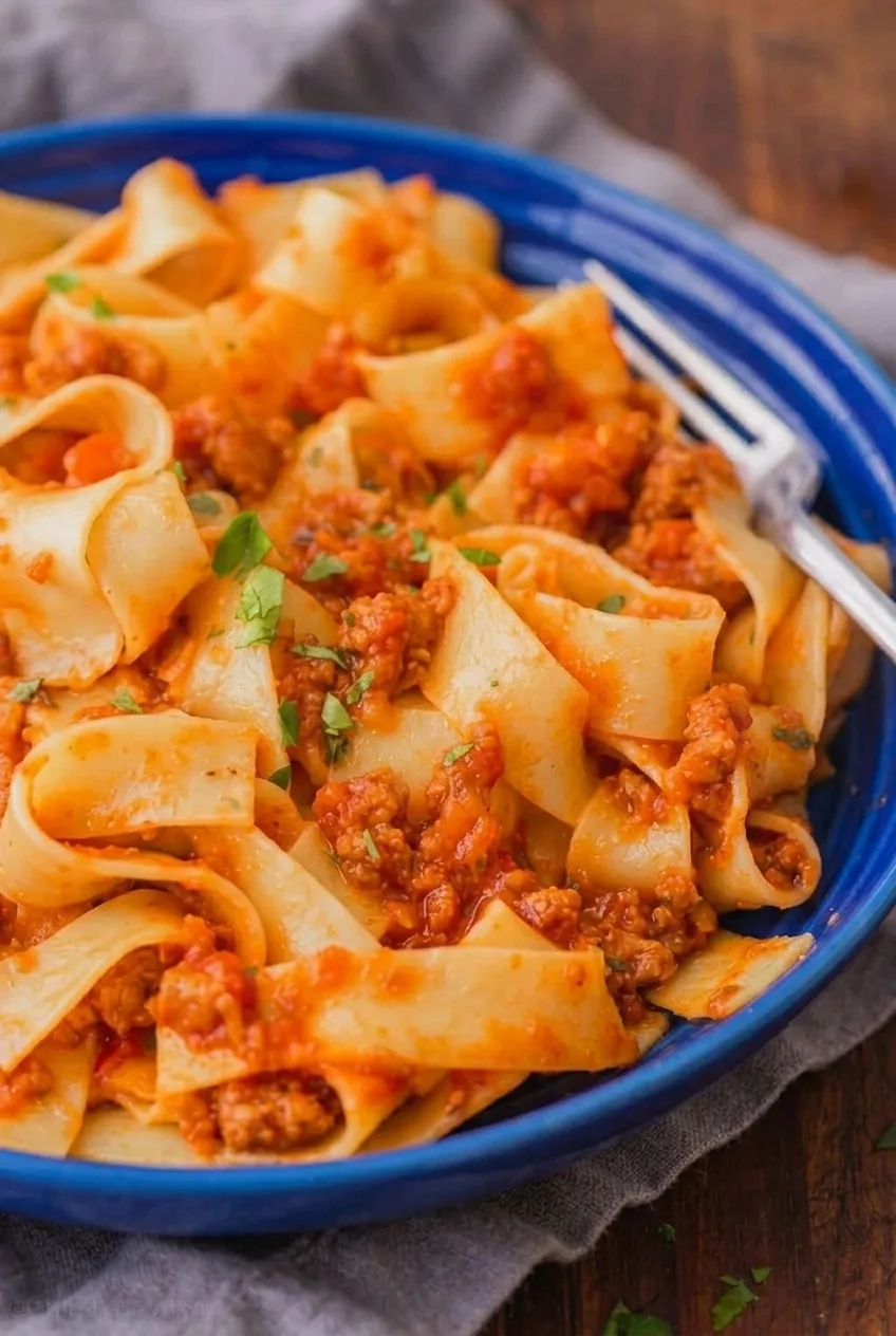 Close detail of thick ground beef Bolognese clinging to broad pappardelle ribbons with parsley flecks.