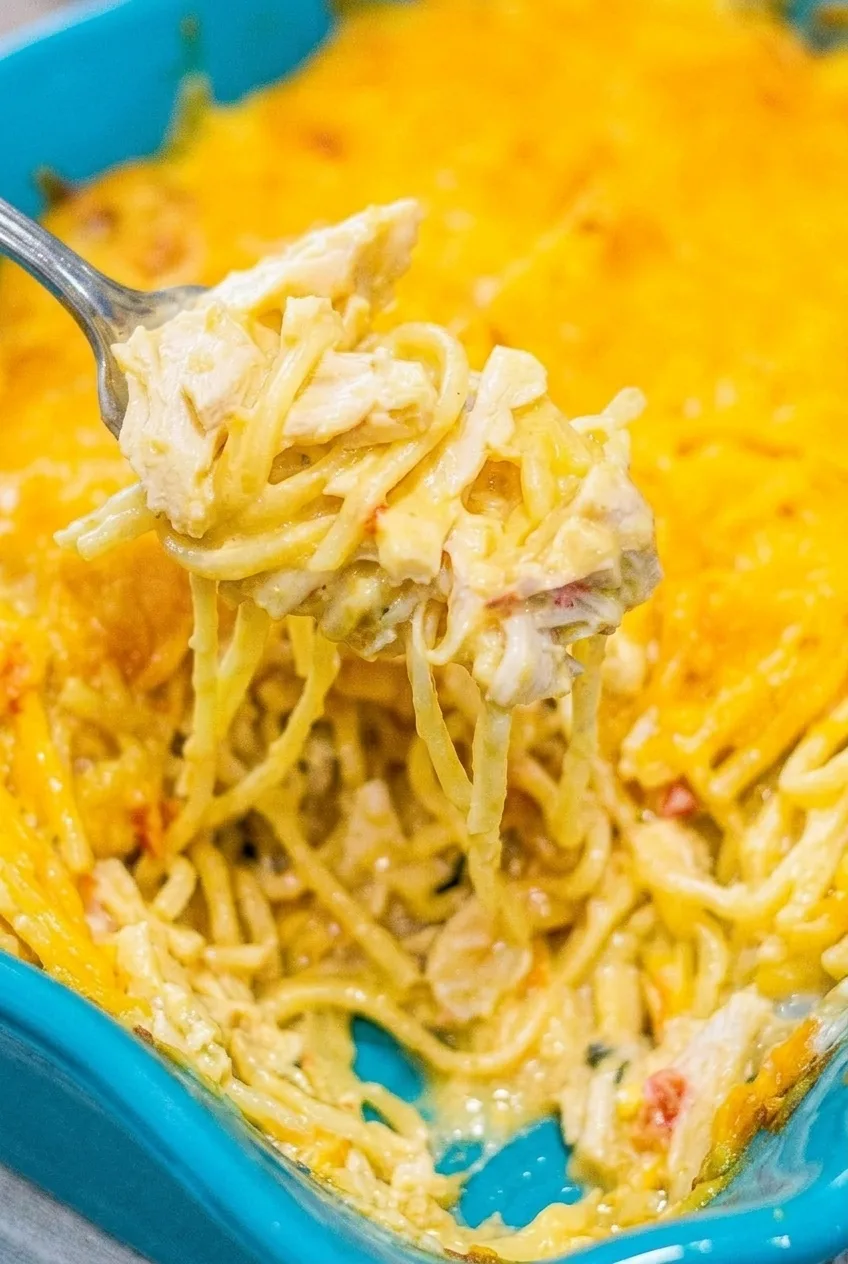 Close-up of creamy chicken spaghetti casserole showing distinct coated noodles, pale chicken pieces, and melted cheddar.