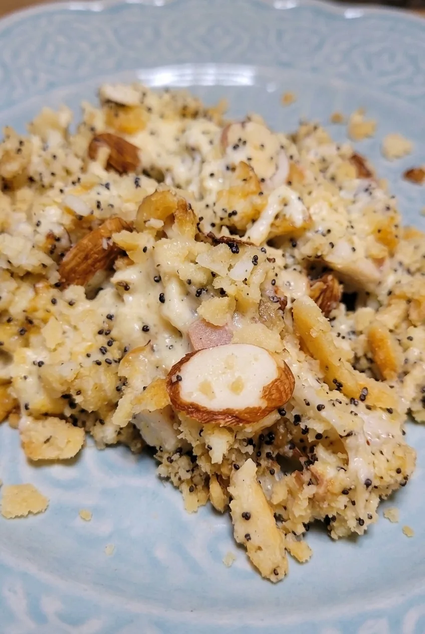 Close detail of creamy chicken pieces, coarse buttery cracker crumbs, black poppy seeds, and sliced almonds.