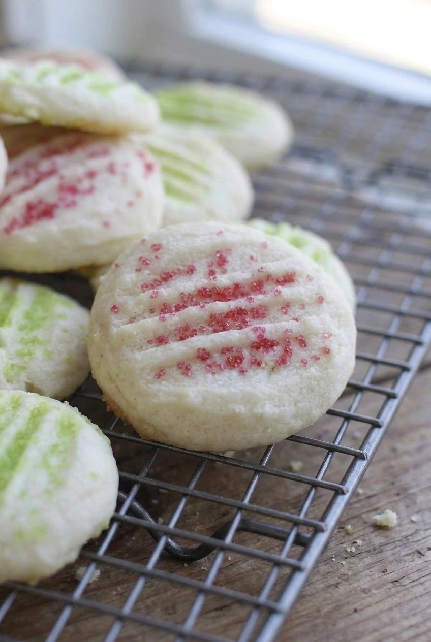 Close-up of a whipped Christmas shortbread cookie showing its delicate crumb, fork grooves, and colored sugar crystals