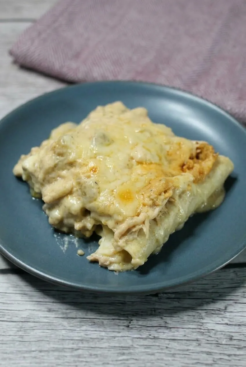 Wider view of two white chicken enchiladas on a blue-gray plate with creamy sauce