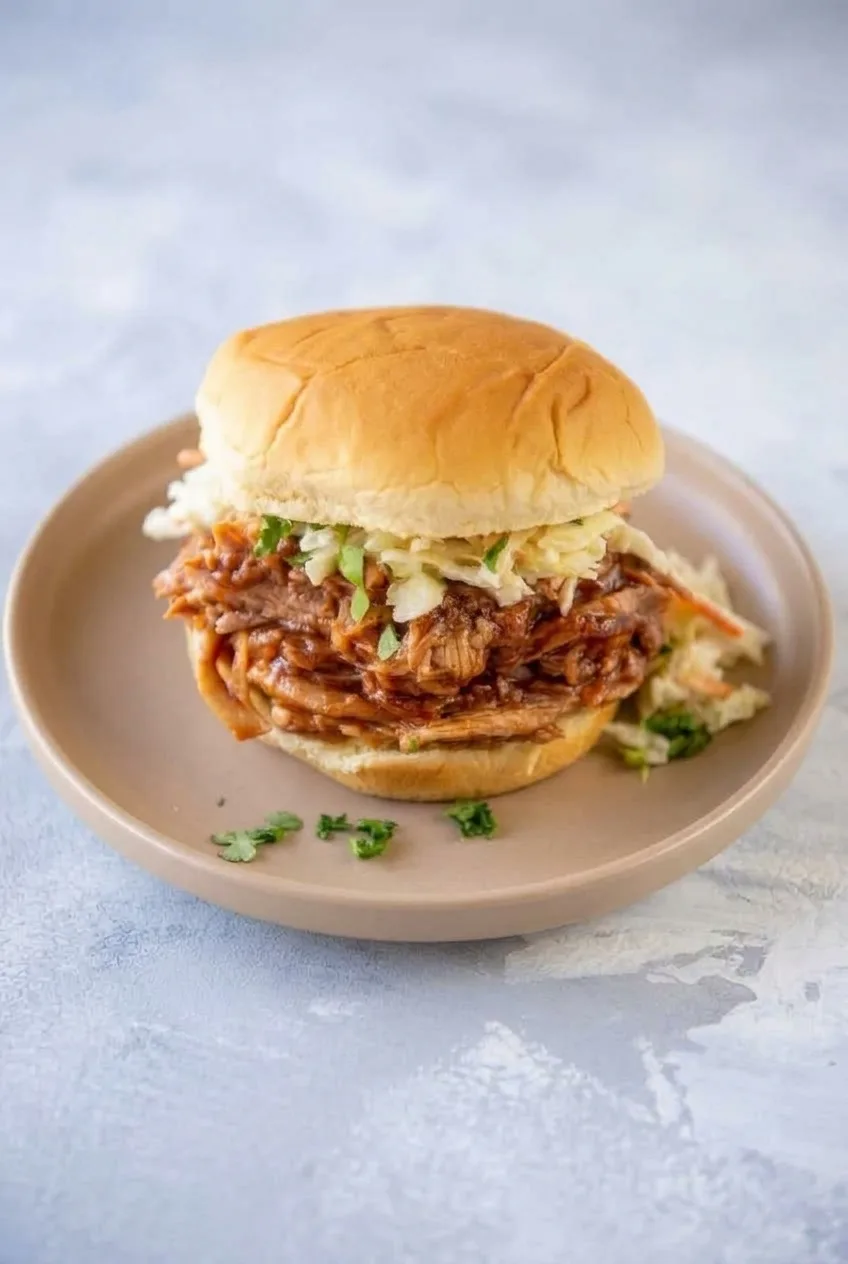 Complete pulled pork and coleslaw sandwich on a plate with the full serving visible