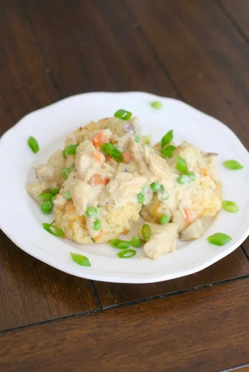 Complete plate of Crock Pot chicken pot pie over biscuits on a dark wooden table