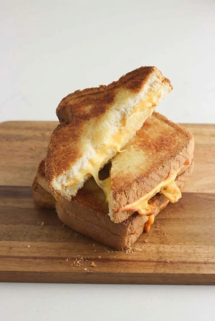Two triangular grilled cheese halves on a wooden board, photographed from farther back