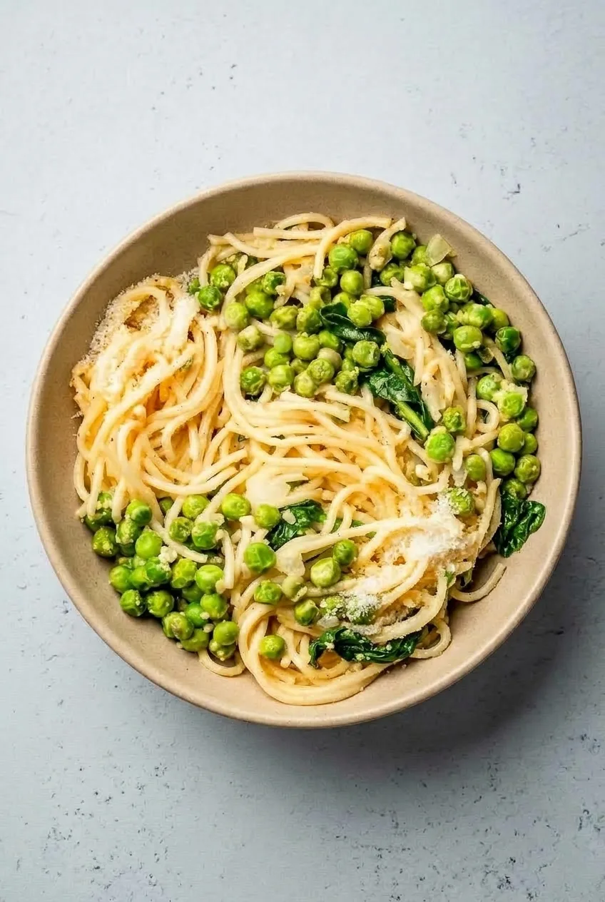 Complete bowl of Parmesan pea spaghetti on a pale gray tabletop, with space around the bowl