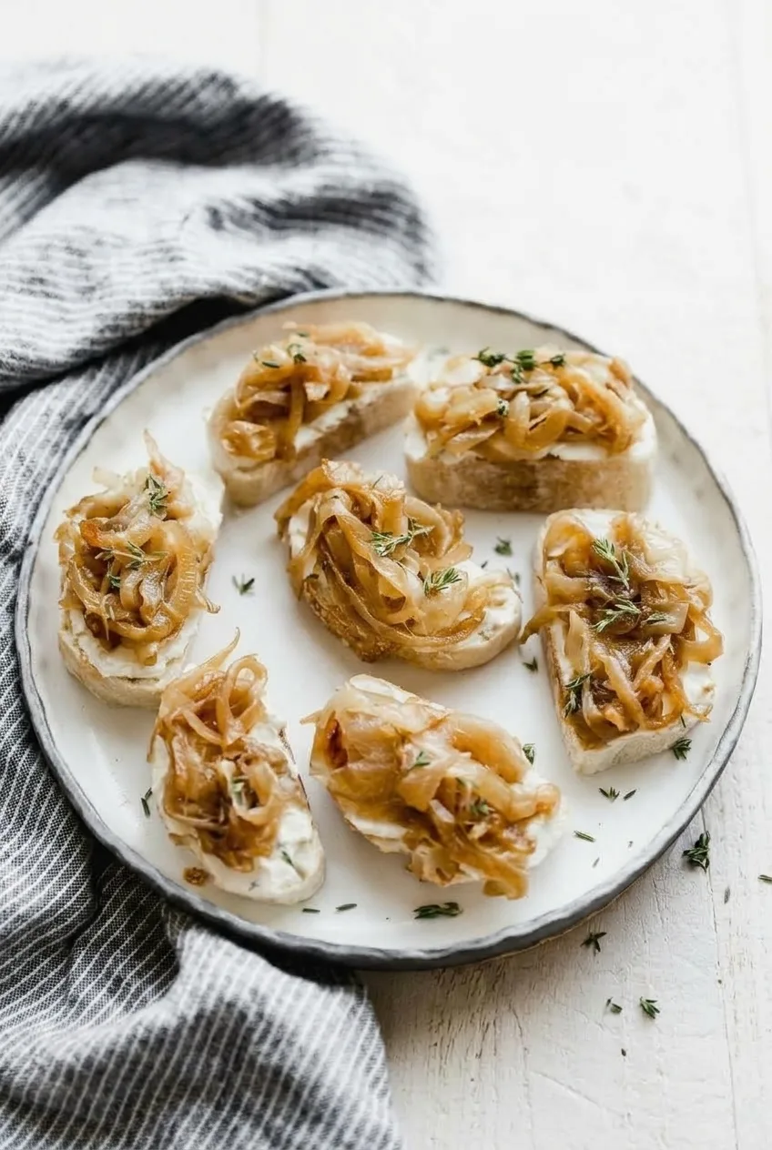 Full plate of caramelized onion and goat cheese crostini on a pale tabletop