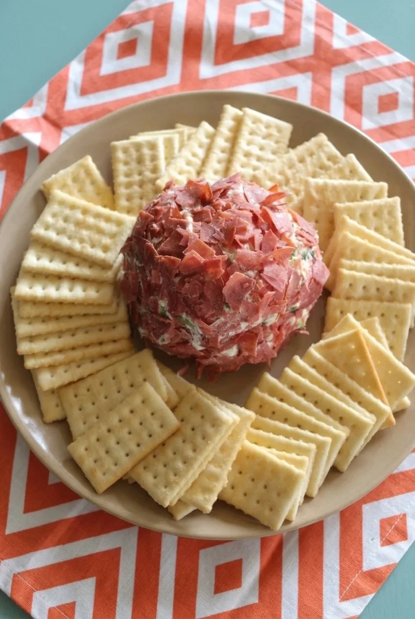 Full plate of smoked salmon cheese ball and square crackers on a patterned tablecloth