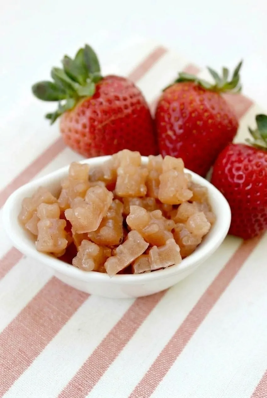 Full white bowl of homemade strawberry-orange fruit snack bears with fresh strawberries nearby