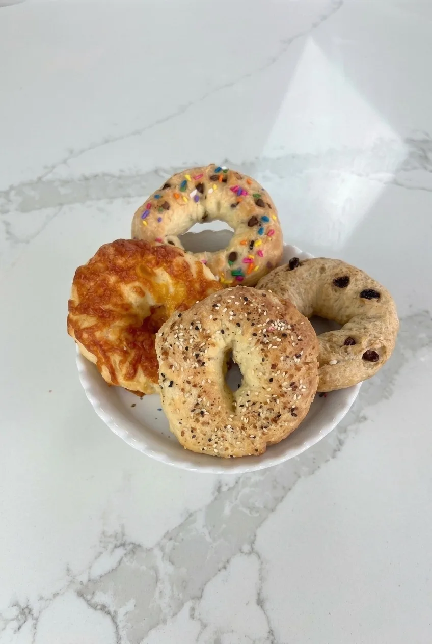 White plate of four differently topped mini protein bagels on a pale marble-look countertop