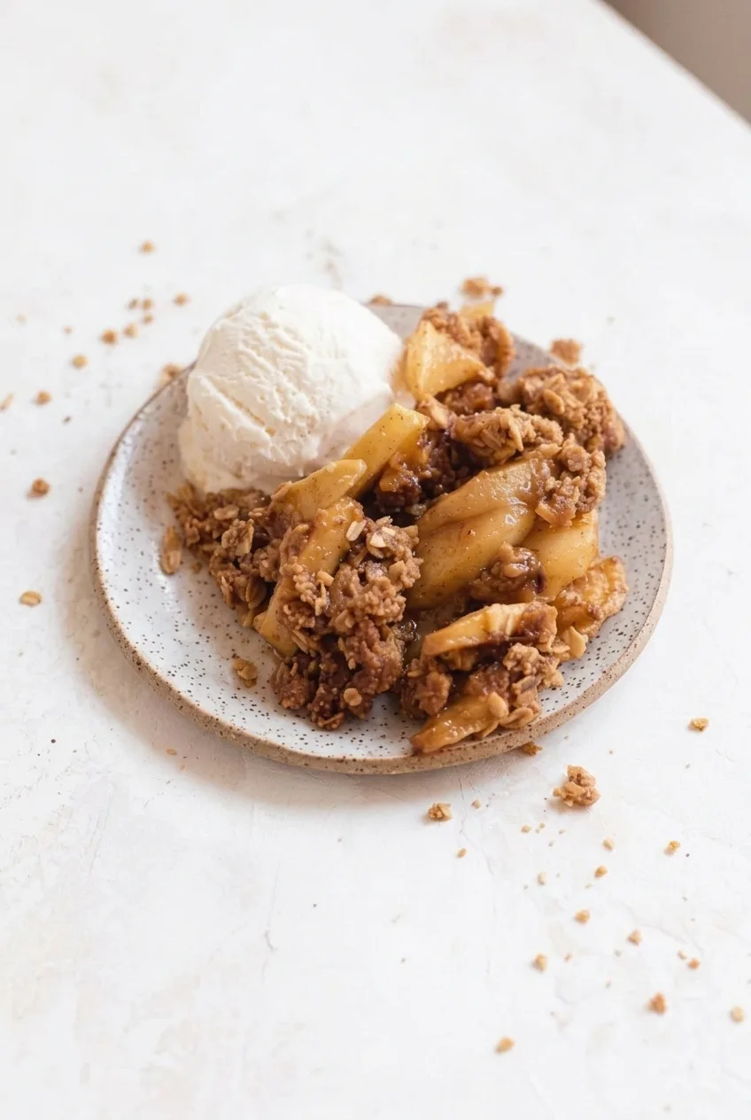 Complete plate of apple crisp and vanilla ice cream on a light tabletop
