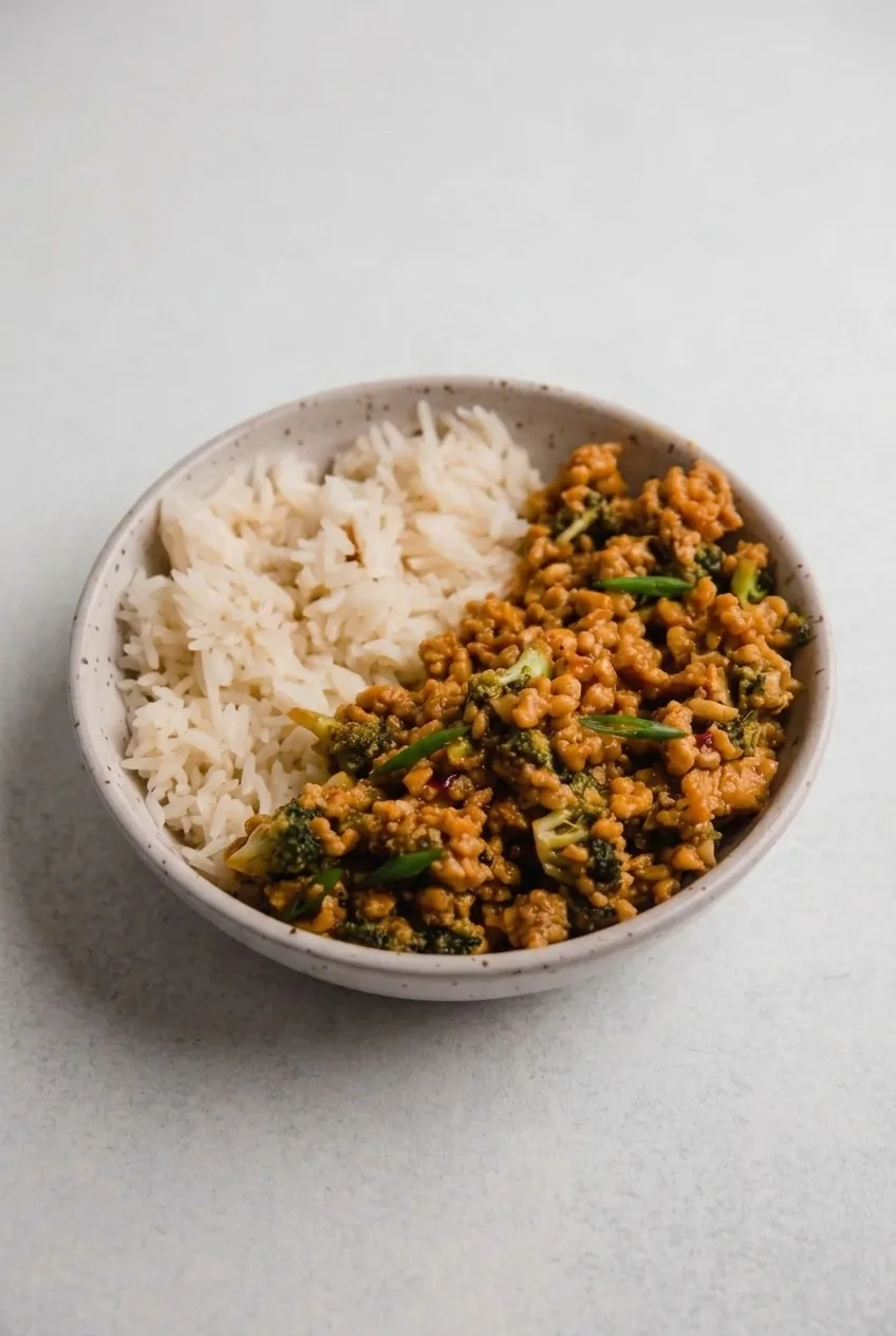 Complete firecracker ground chicken bowl with broccoli and rice on a light neutral tabletop