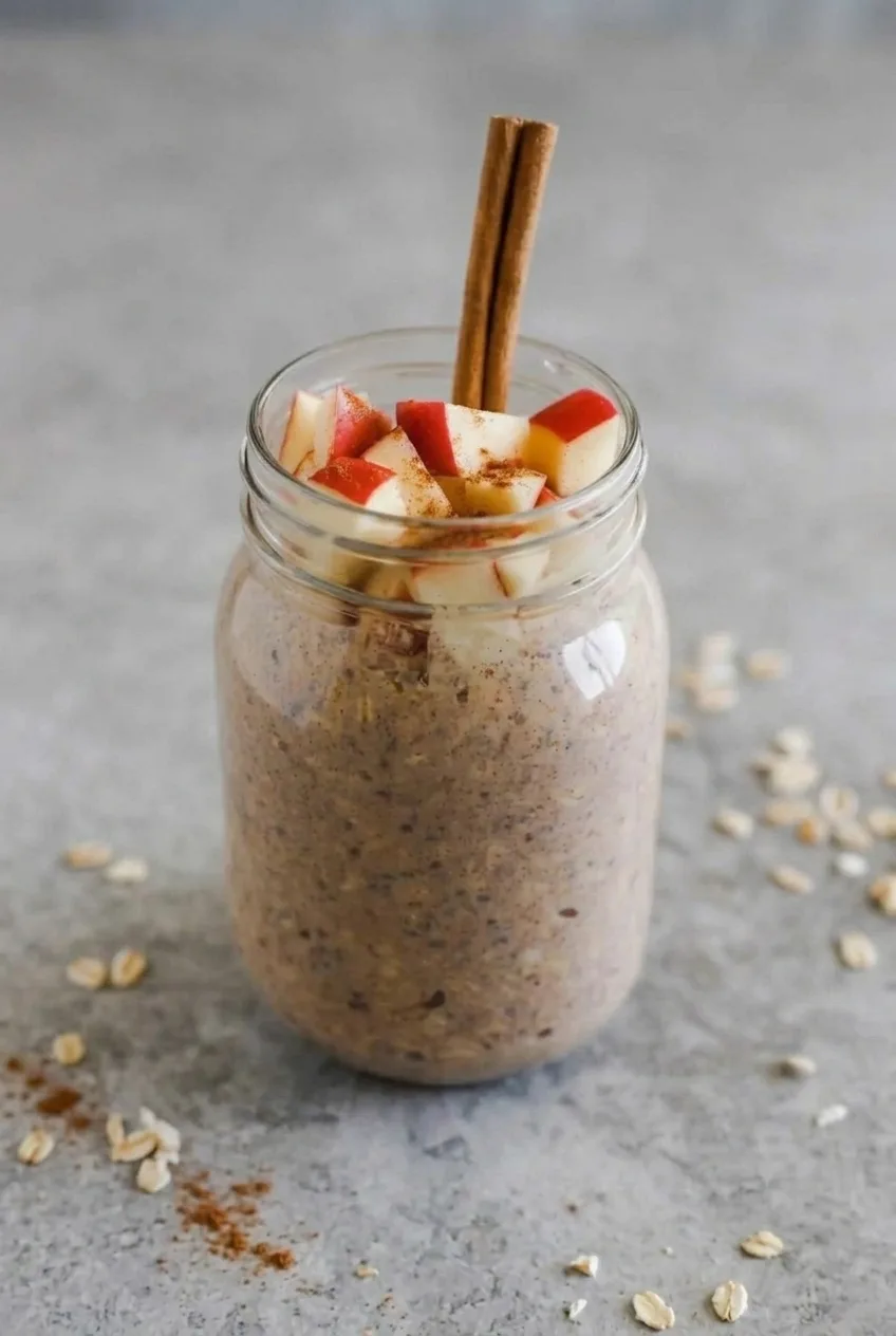 Wider view of a finished jar of apple cinnamon overnight oats on a gray surface
