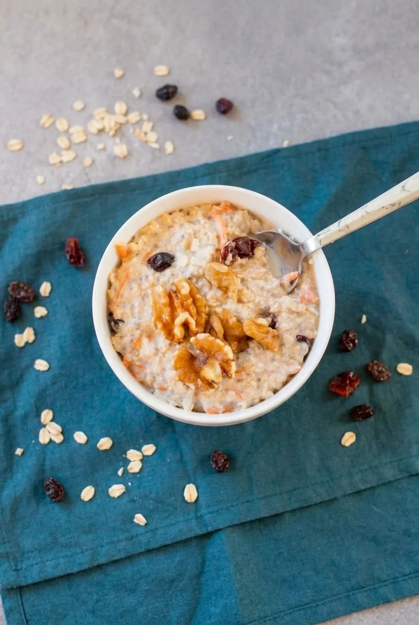 Complete bowl of carrot cake overnight oats with walnuts and raisins on a dark teal cloth