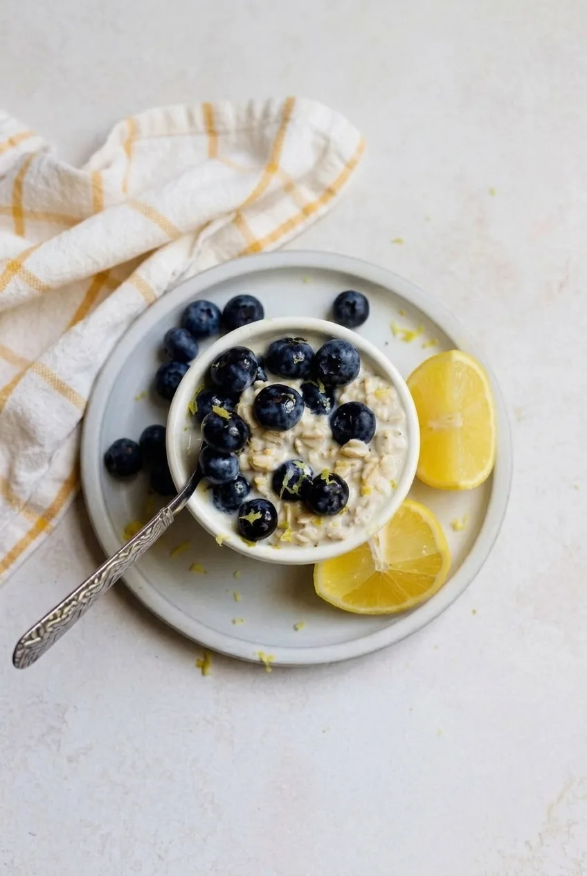 Complete bowl of lemon blueberry overnight oats on a saucer with lemon wedges beside it