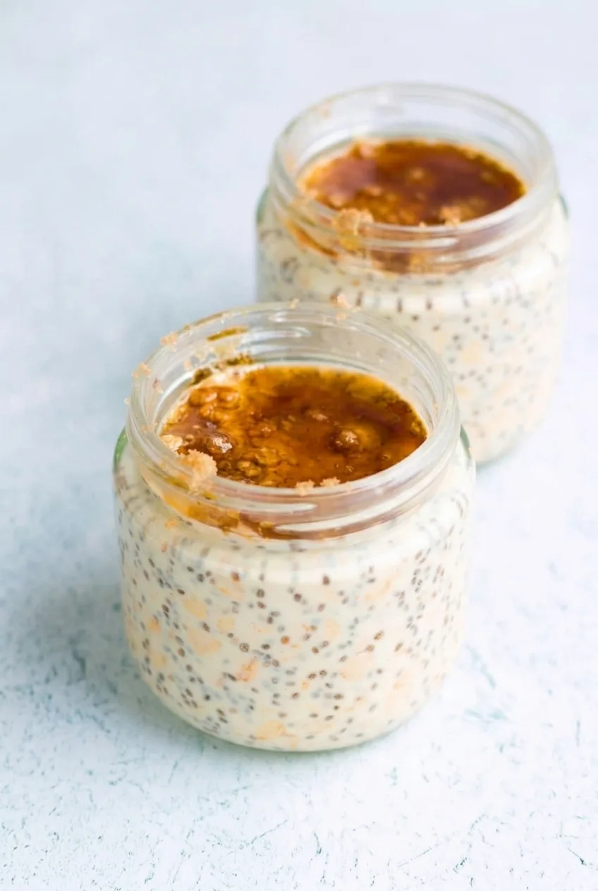 Two finished jars of maple brown sugar overnight oats on a pale surface