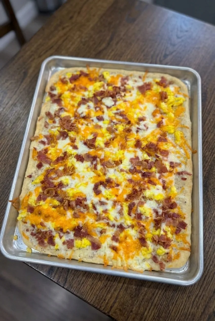 Whole rectangular breakfast pizza on a rimmed baking sheet, viewed with more countertop around it