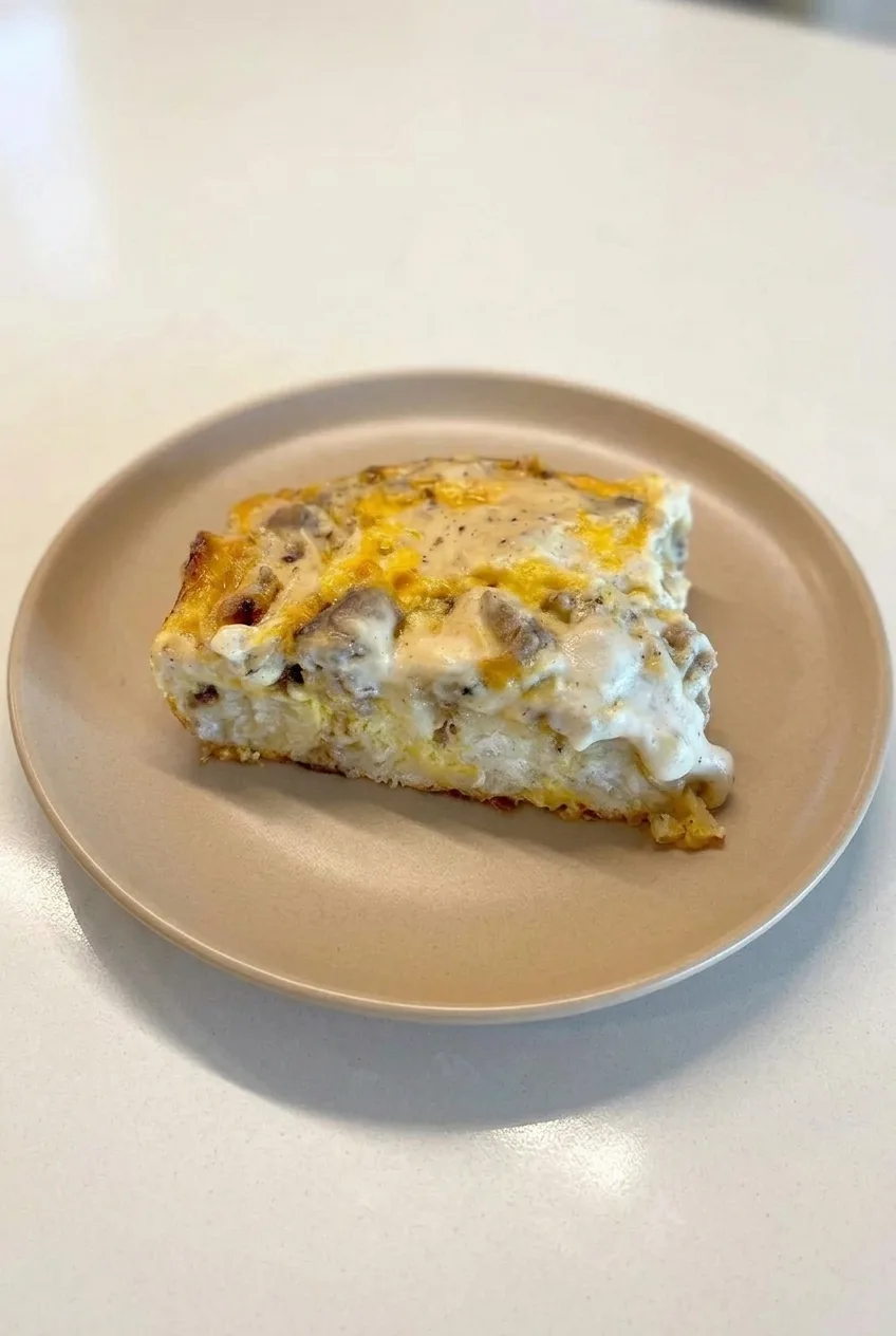 Full plate with a slice of biscuits and gravy casserole, its cut face and gravy-covered top visible