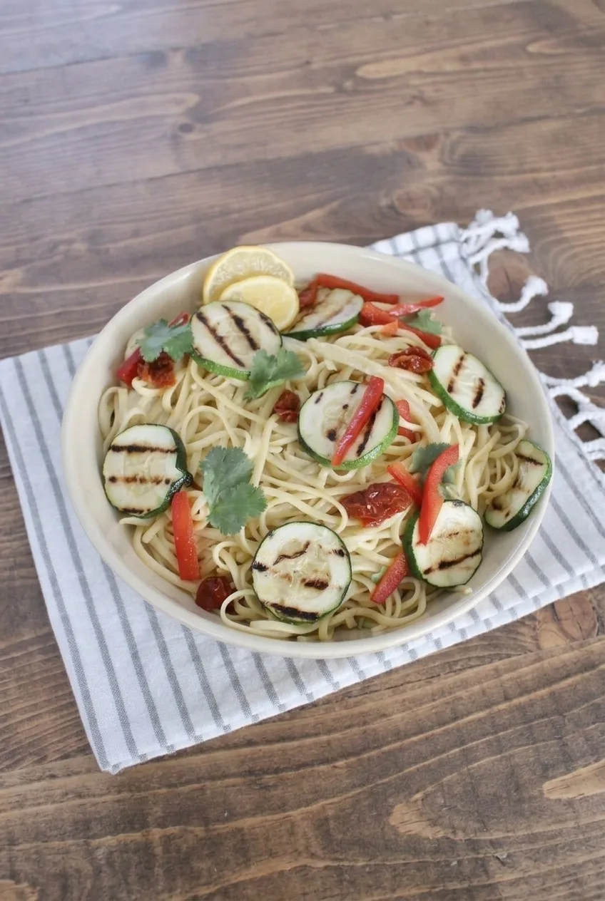 Full bowl of creamy lemon garlic linguine with grilled vegetables and lemon, shown on a rustic wood surface