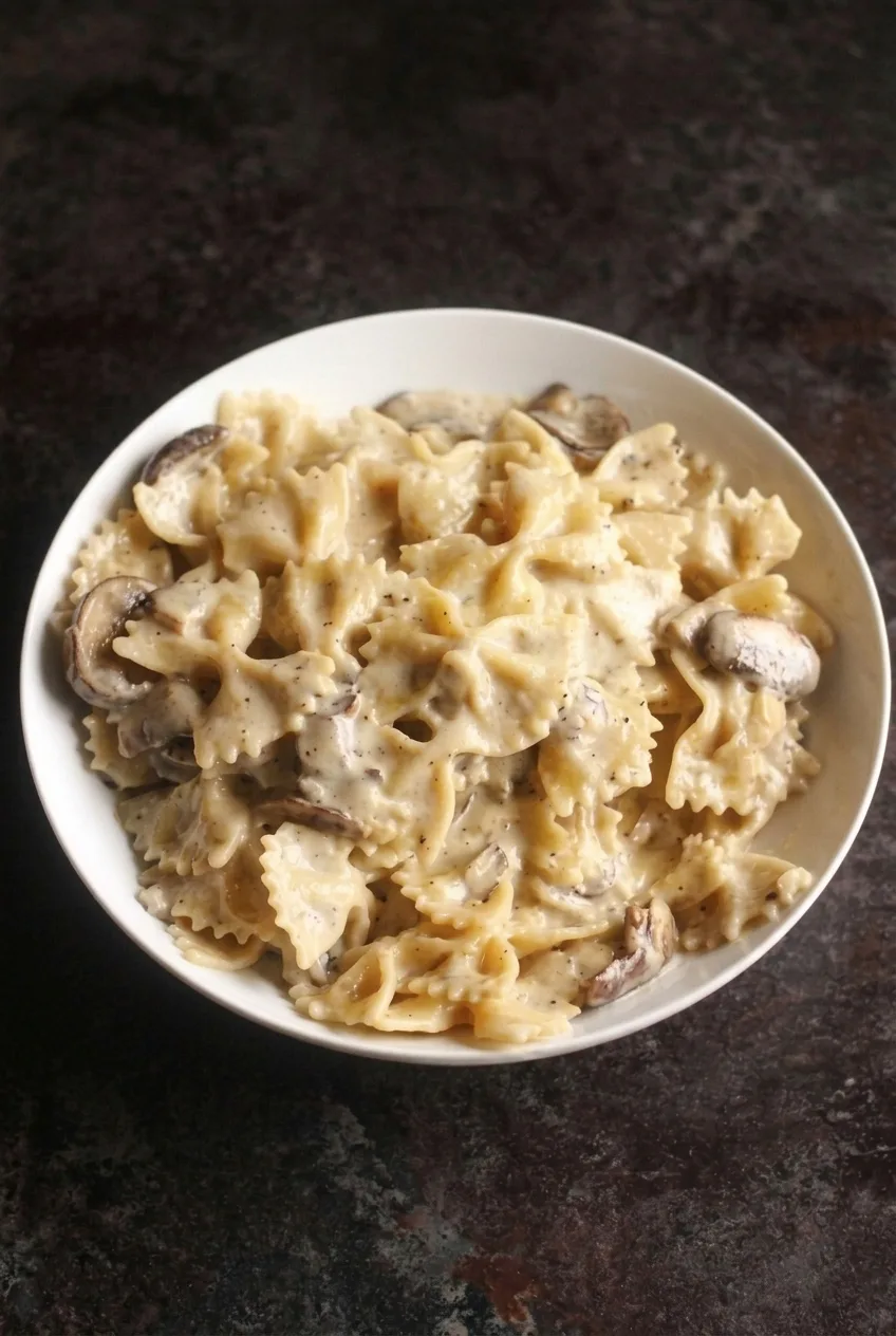 A full bowl of creamy mushroom farfalle centered on a dark countertop with room around it.