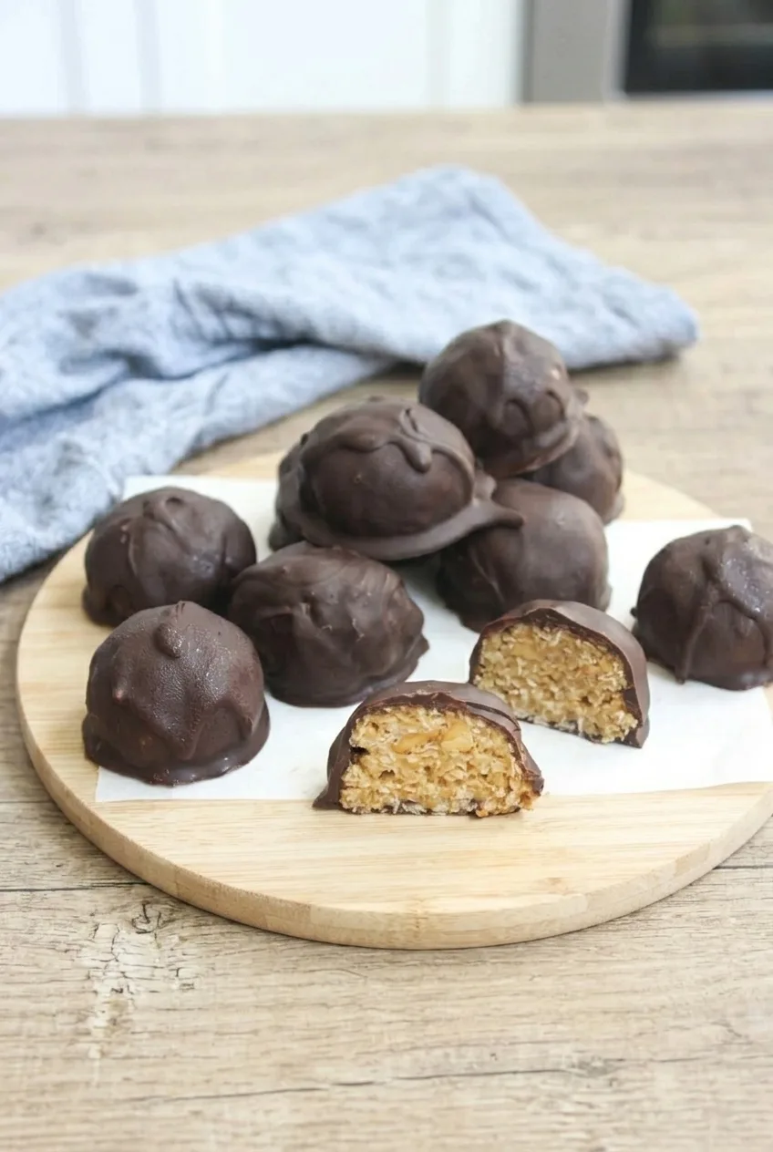 A serving of whole chocolate peanut butter balls with one halved ball on a light wooden board