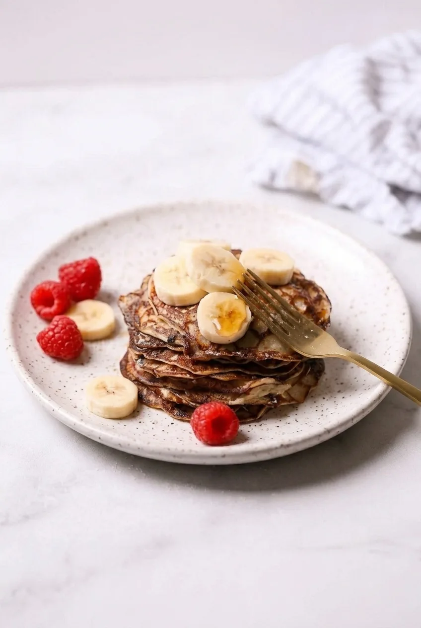 A full plate of thin cottage cheese pancakes stacked with banana, raspberries, and maple syrup