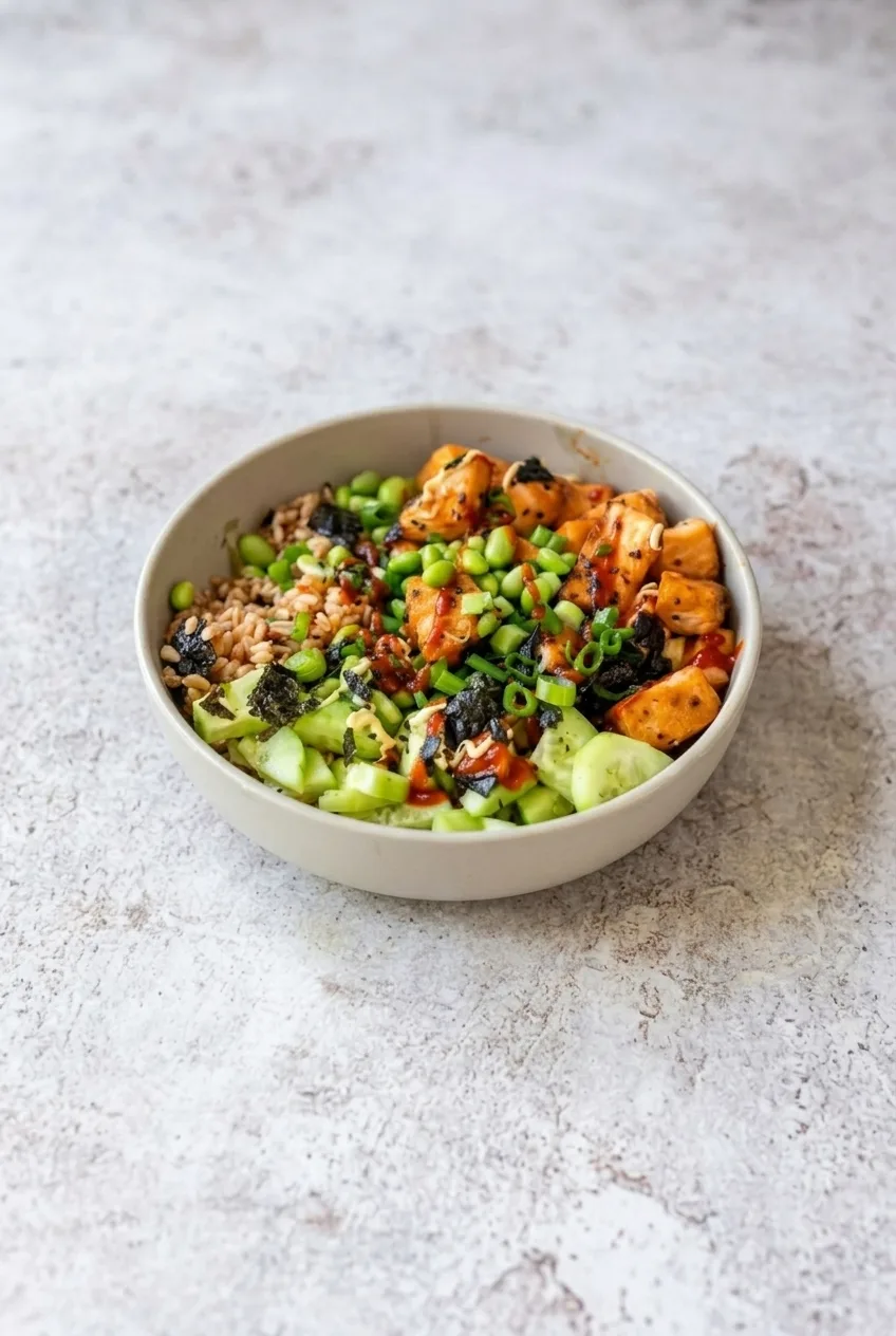 A complete teriyaki salmon rice bowl centered on a pale stone surface, with all toppings and sauces visible