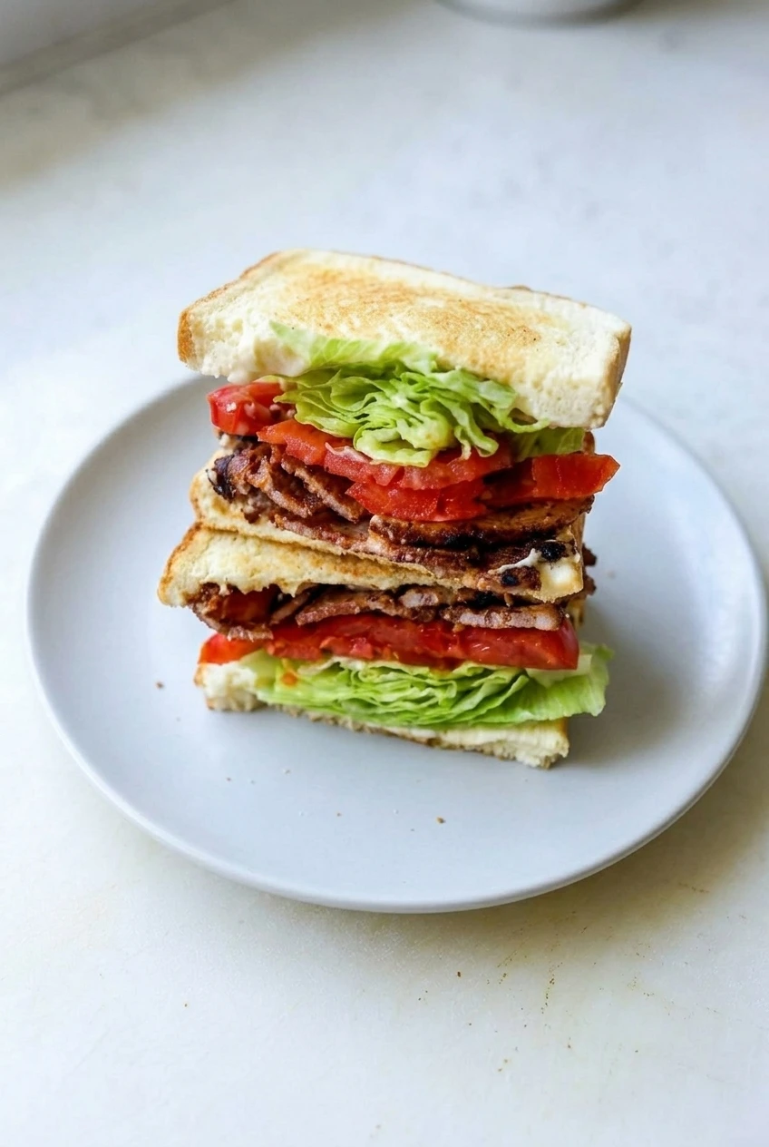 A complete classic BLT, cut and stacked on a light plate with the full serving and surrounding surface visible.