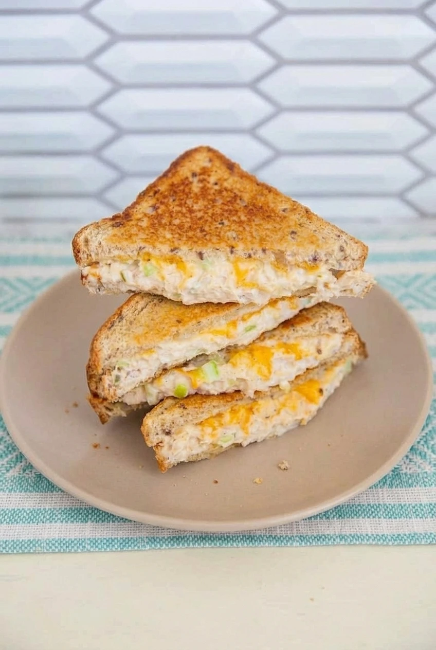 A full plate of diagonal multigrain tuna melt halves in a wider view, with the tuna, celery, and cheddar filling visible.